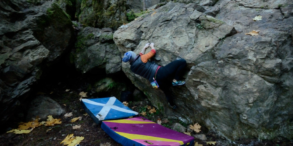 Boulderer on rock face near Cumberland with crash pads below, Comox Valley