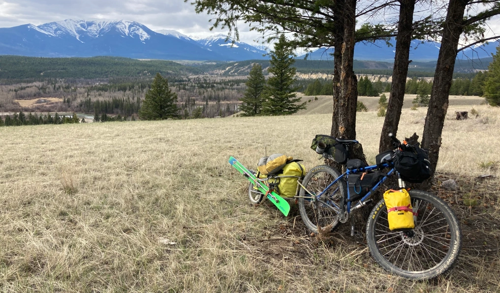 Bikepacking and ski touring setup leaned against trees with BC mountain range in the background 