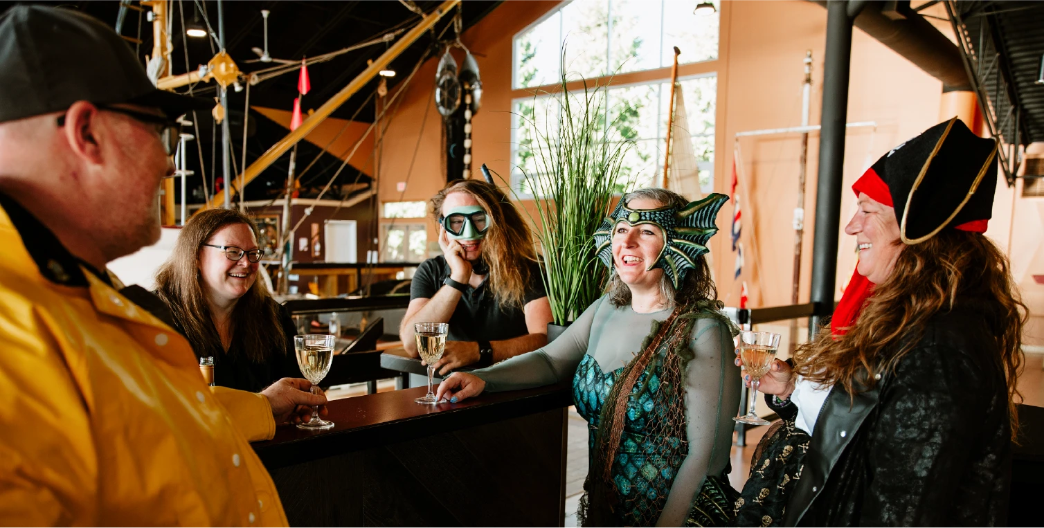 People in maritime costumes including pirate hats and mermaid masks celebrating at Maritime Masquerade fundraising event with champagne