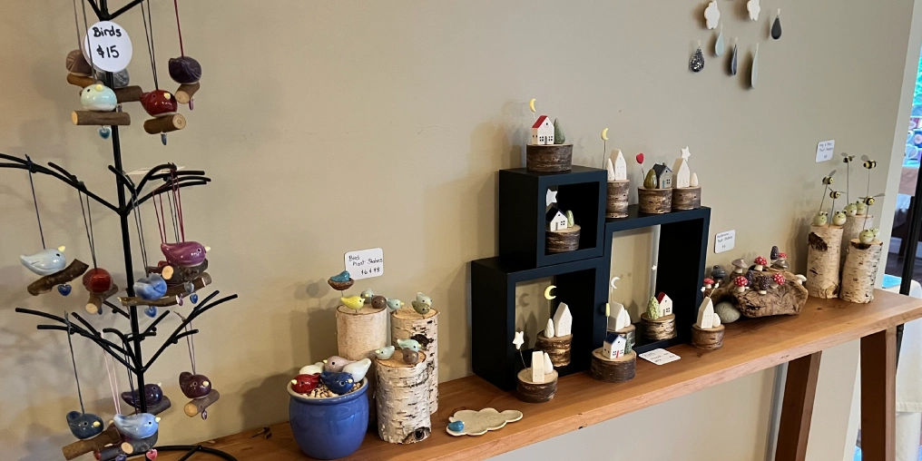Handmade pottery ornaments and figurines displayed at Campbell River Craft Crawl including miniature houses on birch logs and decorative birds