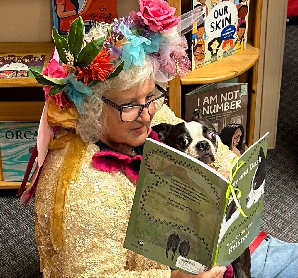 Fairy Dazzle in costume reading a children's book aloud with a Terrier
