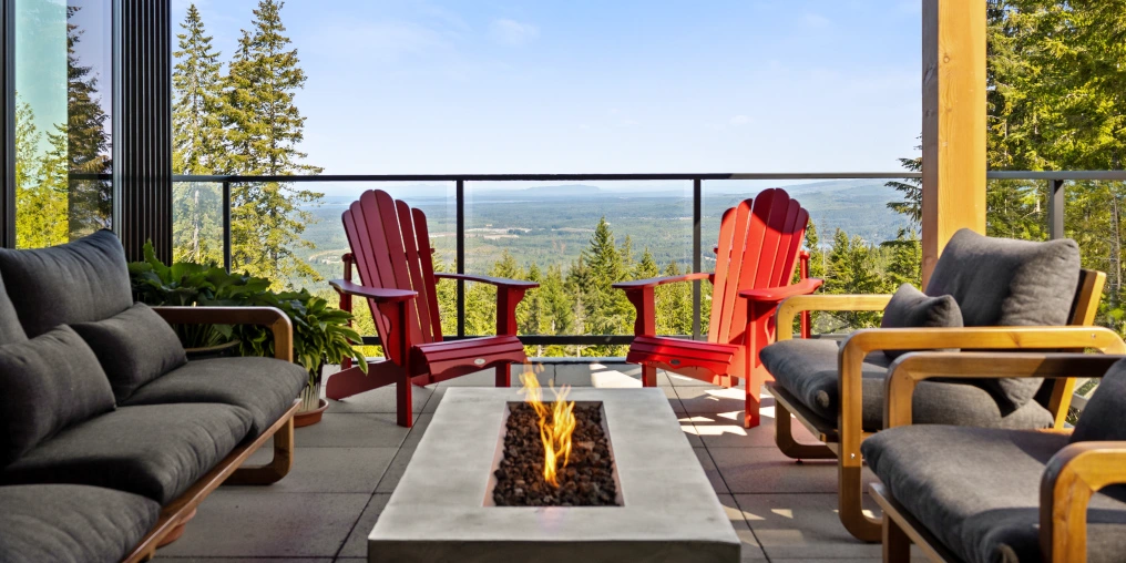 Outdoor deck with red Adirondack chairs and firepit overlooking the Comox Valley from a hilltop acreage