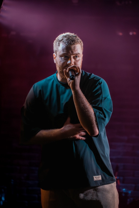 Featured Music: Alick Mac Alick Mac rapping into a microphone under purple stage lighting