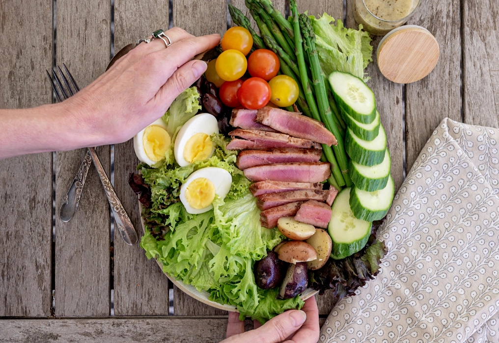 Tune up your diet to turn down your pain Hands plating a colorful anti-inflammatory diet salad with seared tuna, eggs, asparagus, and olives