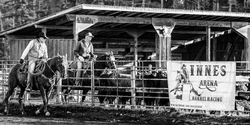 Riders beside the Innes Arena Barrel Racing sign on Vancouver Island