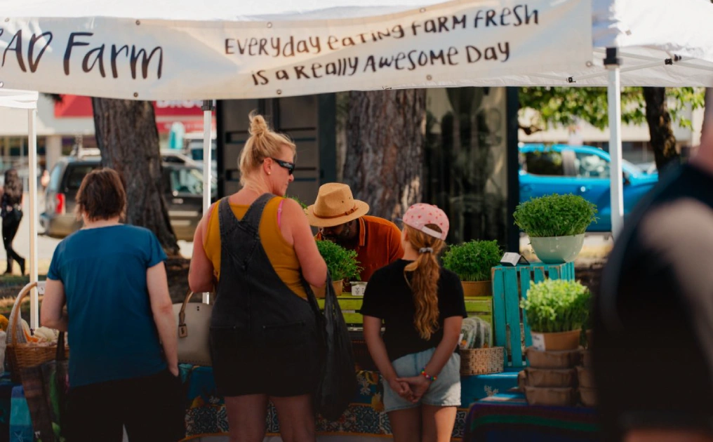 Shoppers at the RAD Farm booth at the Campbell River Farmers Market, banner reads 