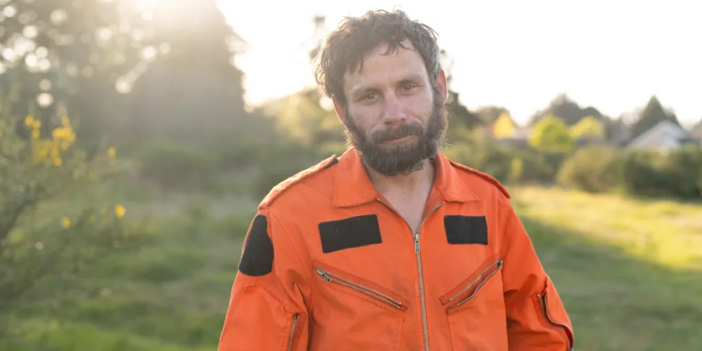 the gift of purpose Highway Jay, a Parksville volunteer known for cleaning up local trails, stands in a sunlit field wearing his orange jumpsuit