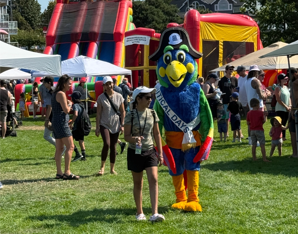 The Nautical Days mascot walks with a young festival-goer past the midway games