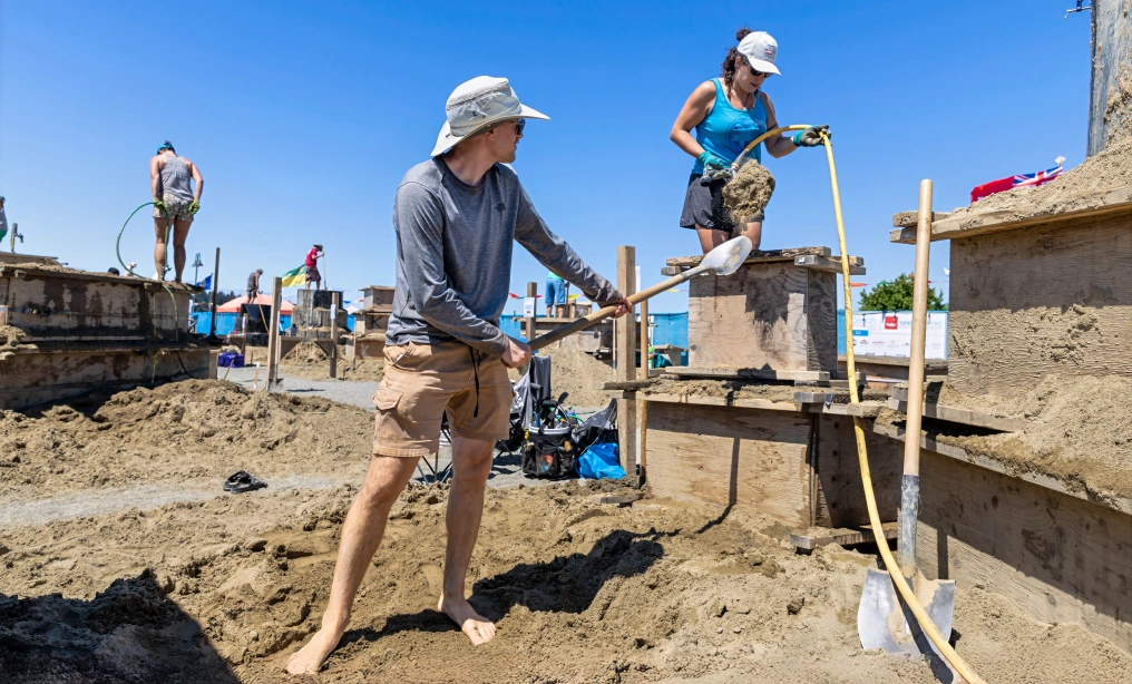 The life of an artist and the legacy of our local competition Sand sculptors packing wet sand into a wooden form at a beach competition