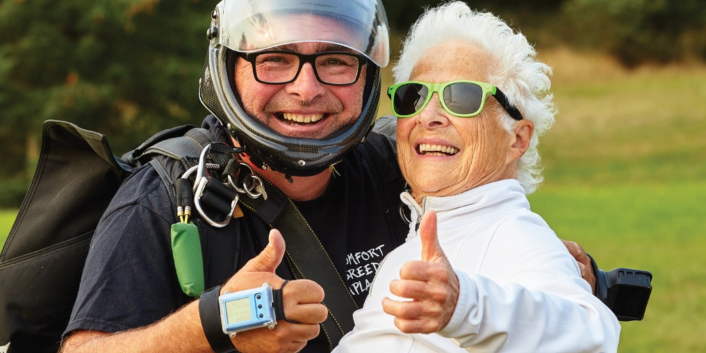 Celebrating 80 years with a tandem skydive Jill and her tandem instructor give a thumbs up after landing safely from her 80th birthday skydive