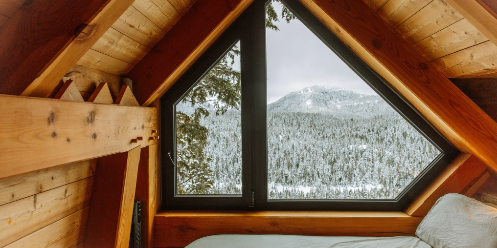 Building Basecamp Triangular bedroom window overlooking snow-covered mountains at the Mount Washington cabin