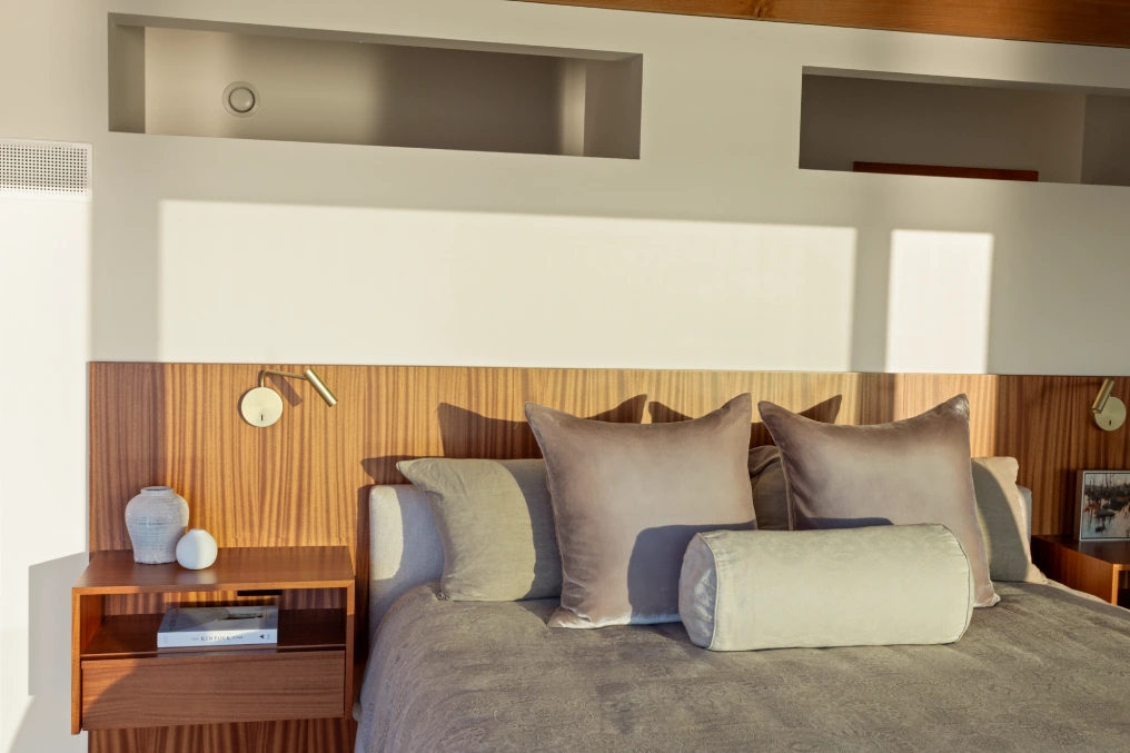Capturing the perfect light at a special house on Cortes Island Close-up of a bedroom headboard with wood paneling, reading sconces, and velvet pillows in warm neutral tones