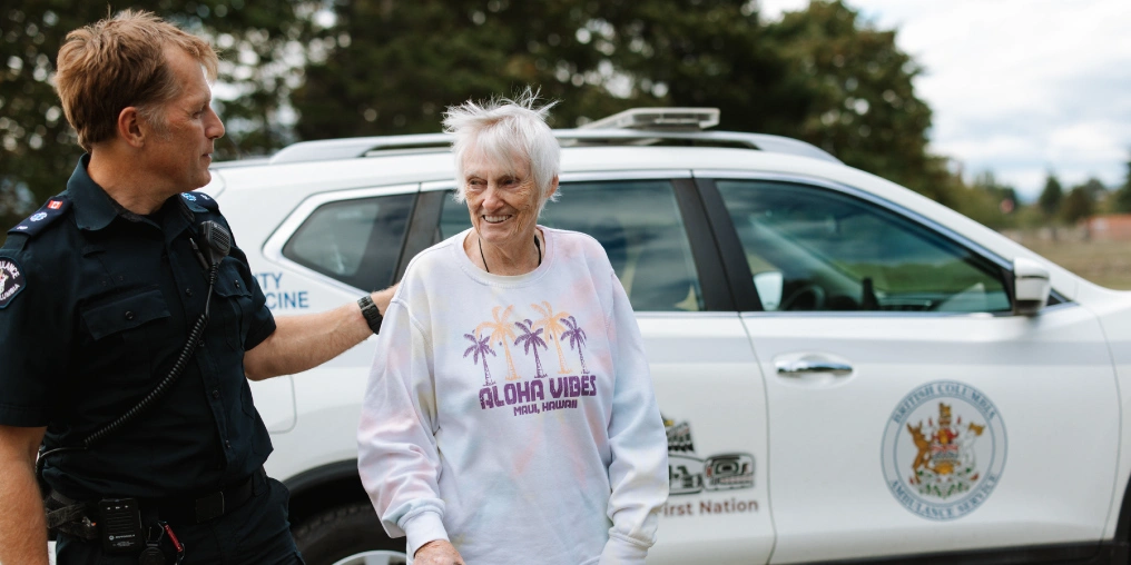 Bridging gaps with community paramedicine A community paramedic in uniform rests a hand on the back of a smiling older woman beside a white paramedic SUV
