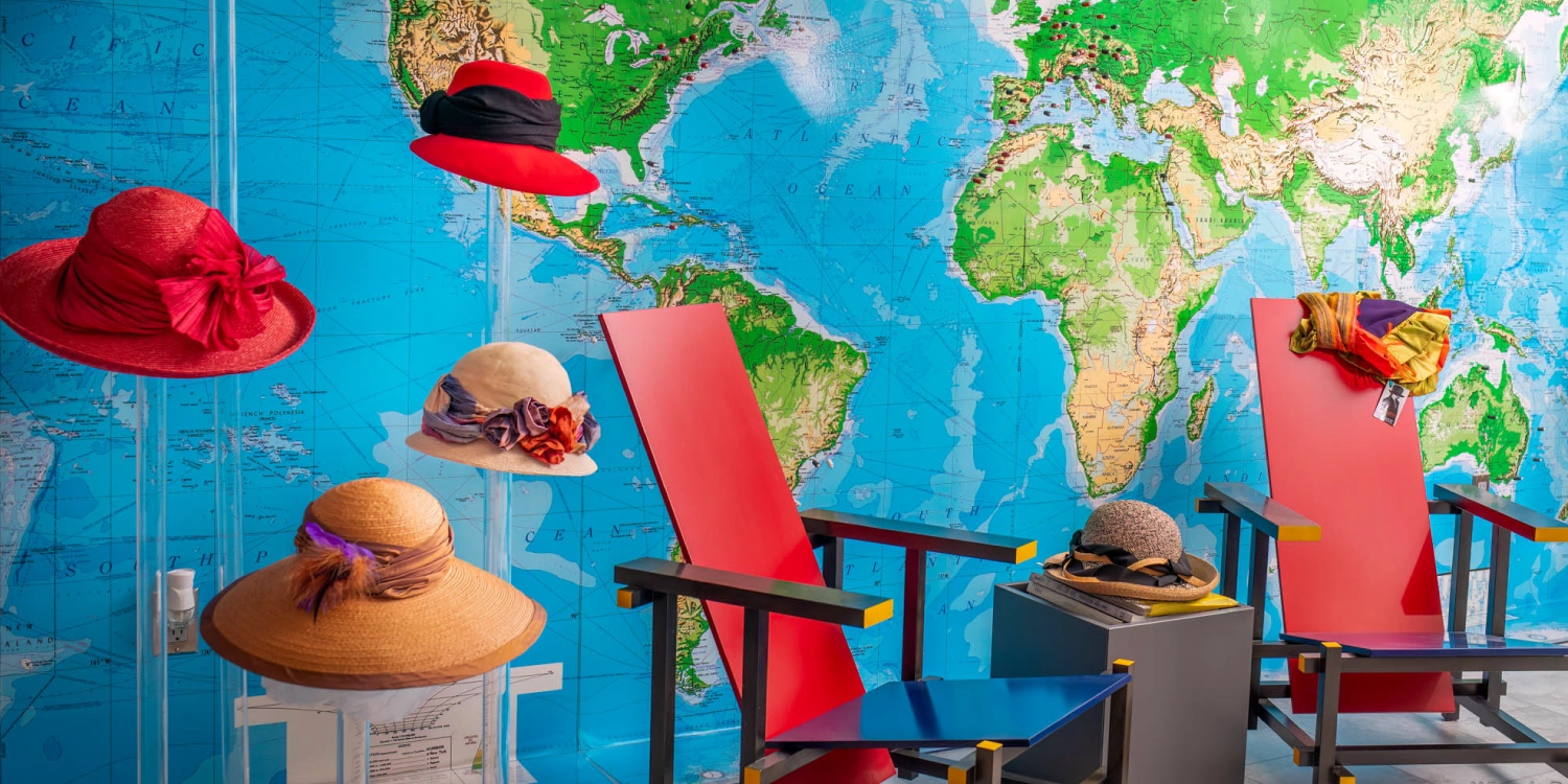 handmade-hats-world-map-display Handmade straw and felt hats displayed in front of a world map mural, beside two red and blue chairs