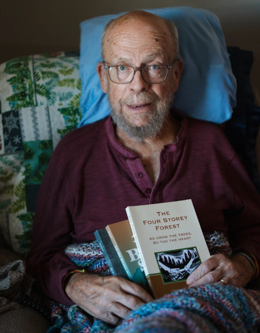 Harold Macy in bed holding the books he has written