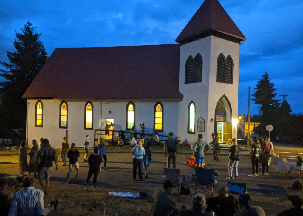 Weird Church at dusk with its arched windows glowing as people gather on the grounds outside