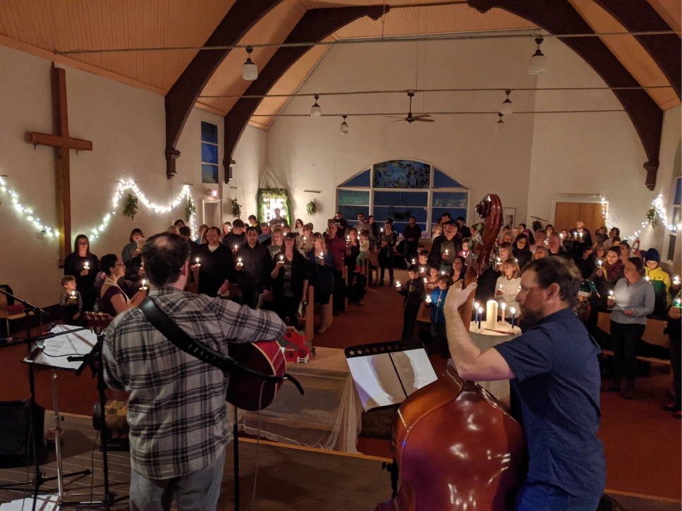 People holding lit candles inside Weird Church in Cumberland as a guitarist and upright bass player lead music from the front